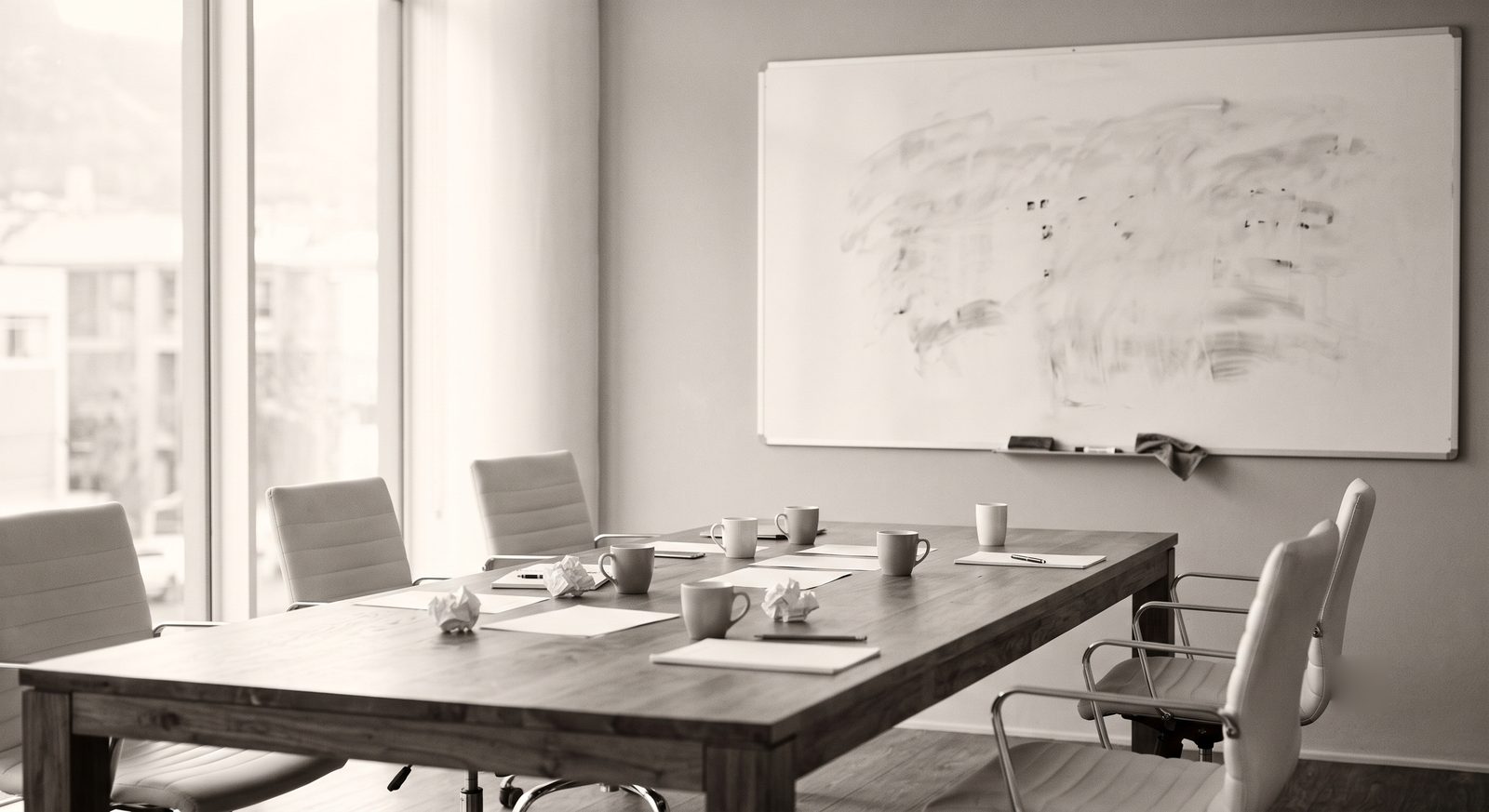 An empty meeting room after a meeting: chairs pushed back, a half-erased whiteboard, cold cups on the table.